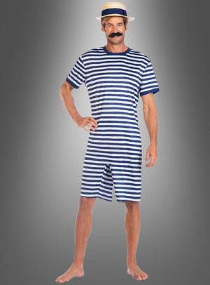 Ein Mann steht barfuß vor einem grauen Hintergrund mit Farbverlauf und trägt den „Gestreiften Schwimmanzug der 20er Jahre“ – einen blau-weiß gestreiften kurzärmeligen Strampler –, dazu einen Strohhut und einen falschen Schnurrbart.