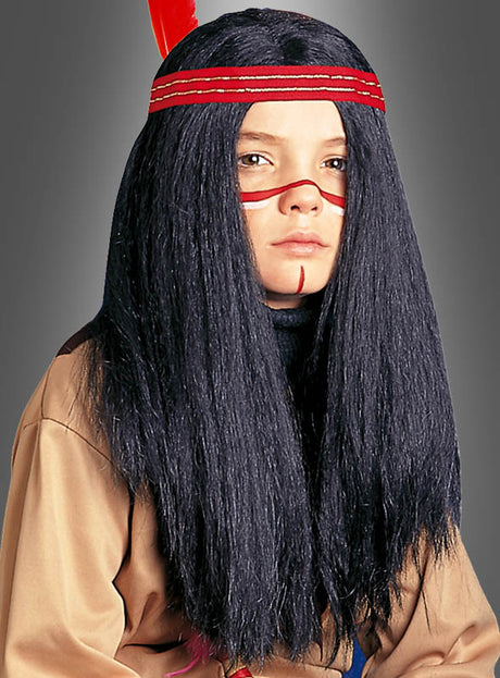 Ein Kind trägt die „Indianer-Perücke für Kinder“ – eine lange schwarze Perücke, die zu einer Indianerfrisur mit rotem Stirnband gestylt ist – sowie hellbraune Kleidung, rote Gesichtsbemalung über den Augen und eine vertikale rote Linie am Kinn, vor einem grauen Hintergrund.
