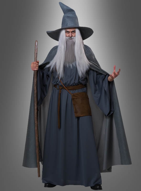 Eine Person im „Magischer Zauberer“-Kostüm Deluxe – mit langem grauen Bart, spitzem Hut, Umhang und Zauberstab – steht vor einem Hintergrund mit Farbverlauf; perfekt für jede Fantasy-Veranstaltung.