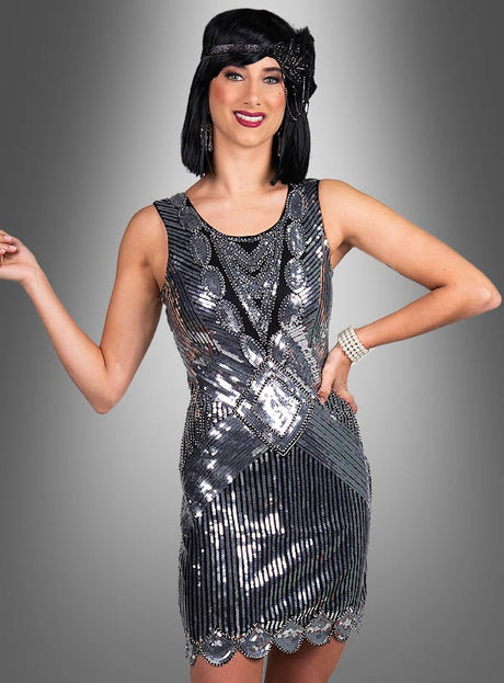 Eine Frau, die das „Premium Paillettenkleider Ruby“ trägt – ein ärmelloses, silbernes Paillettenkleid im Flapper-Stil der 20er Jahre – sowie ein schwarzes Stirnband, posiert vor einem grauen Hintergrund mit Farbverlauf.