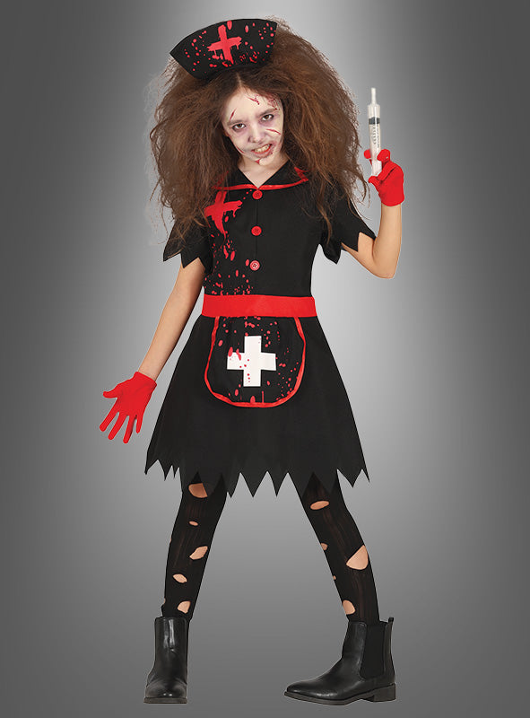 Ein Kind im „Zombie-Krankenschwester“-Kostüm für Kinder, bestehend aus einem schwarzen Kleid mit auffälligen roten und weißen Details, wilder Frisur, Gesichts-Make-up, roten Handschuhen und einer Spritze in der Hand. Dieses blutbespritzte Kinderkostüm hebt sich lebhaft vom grauen Hintergrund ab.