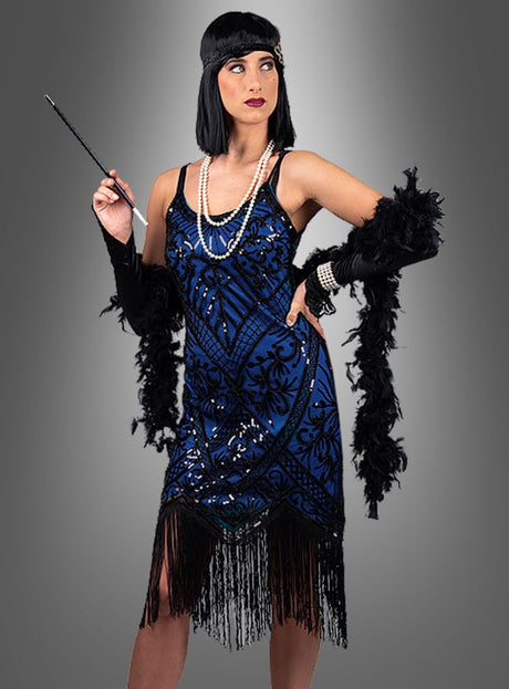Eine Frau in einem glamourösen blauen Glamouröses Paillettenkleid im Cleo-Flapper-Stil mit Fransen, einer schwarzen Federboa, einem Stirnband und Perlenketten, die eine Zigarettenspitze in der Hand hält, posiert vor einem grauen Hintergrund mit Farbverlauf.