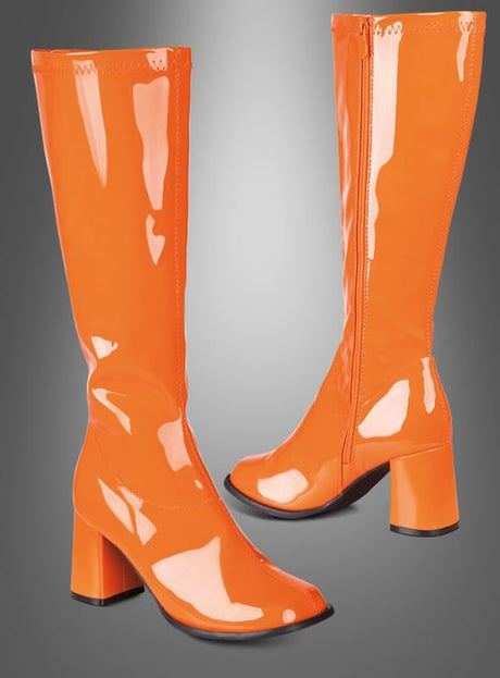 Ein Paar glänzende orangefarbene Lackstiefel im Stil der 70er Jahre – kniehoch, mit Blockabsatz und seitlichen Reißverschlüssen – wird vor einem grauen Hintergrund mit Farbverlauf präsentiert. Diese Stiefel eignen sich ideal als Damenschuhe für ein Disco-Kostüm und setzen ein markantes Statement im Retro-Chic, inspiriert von der gewagten Mode der 1970er Jahre.