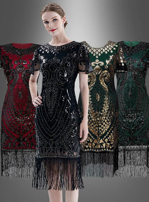 Eine Frau präsentiert das schwarze 20er-Jahre-Kleid „Grace“ mit kurzen Ärmeln und Pailletten – ein klassisches, kurzärmeliges Flapper-Kleid mit Pailletten und Fransen, ideal für eine Charleston-Party –, während ähnliche Modelle in Rot, Dunkelgold und Grün auf Schaufensterpuppen vor einem grauen Hintergrund ausgestellt sind.