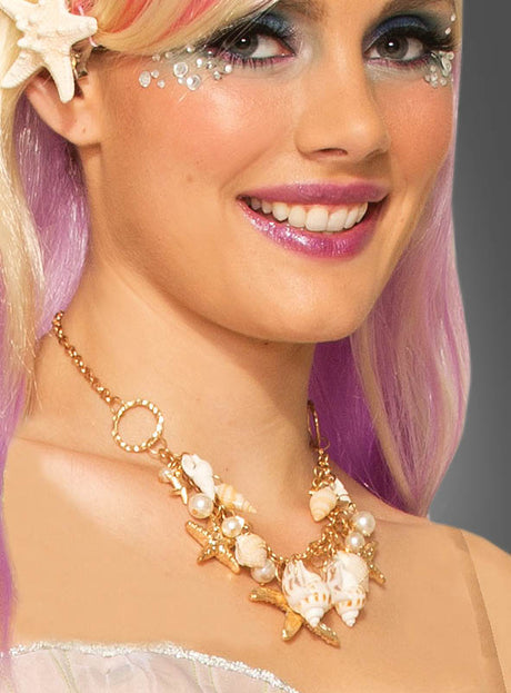 Eine Frau mit hellviolettem Haar trägt eine goldene Halskette „Muscheln Meerjungfrau“, die mit Muschel- und Perlenanhängern verziert ist. Dazu passen ihr schimmerndes Make-up und dekorative Gesichtssteine – ein Look, der perfekt zu jedem Meerjungfrau-Kostüm passt.
