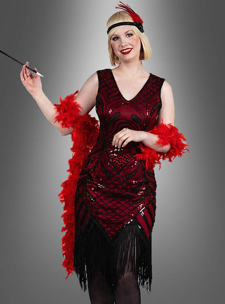 Eine Person in einem exklusiven 20er-Jahre-Flapper-Kleid namens „Vivian“ mit Fransen, die eine lange Zigarettenspitze in der Hand hält und ein rotes Stirnband mit Federn sowie eine Boa trägt, steht vor einem grauen Hintergrund.