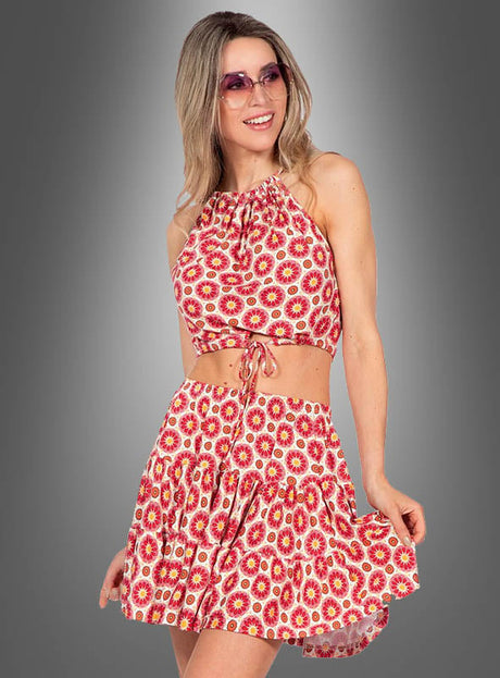 Eine Frau, die das „Sommer Rock und Oberteil Boho Outfit“ trägt – ein ärmelloses, rot-weiß gemustertes Crop-Top mit einem dazu passenden Rock –, kombiniert es mit einer Sonnenbrille und lächelt vor einem grauen Hintergrund.