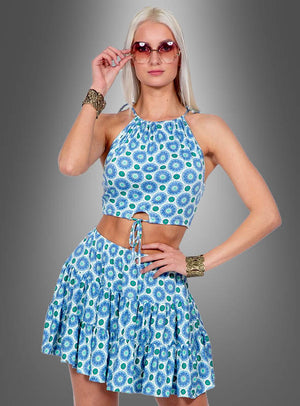 Eine Frau präsentiert das „Sommer Rock und Oberteil Boho“-Outfit, bestehend aus einem blau gemusterten, kurz geschnittenen Neckholder-Oberteil mit passendem Rüschenrock, ergänzt durch eine Sonnenbrille und goldene Armbänder, vor einem grauen Hintergrund mit Farbverlauf.