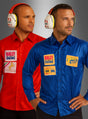 Zwei Männer stehen nebeneinander, jeder trägt ein rotes oder blaues Formel-1-Rennfahrer-Shirt zum Sonderpreis, das mit Rennsport-Aufnähern verziert ist, sowie einen Gehörschutz; sie blicken vor einem grauen Hintergrund leicht in entgegengesetzte Richtungen.