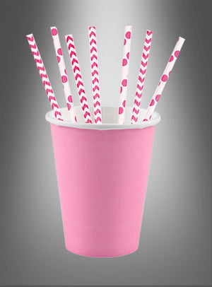 In einem rosa Pappbecher befinden sich sieben Papierstrohhalme in Rosa und Weiß, die jeweils ein einzigartiges Muster wie Streifen, Zickzackmuster und Tupfen vor einem grauen Hintergrund mit Farbverlauf aufweisen. Diese umweltfreundlichen Papierstrohhalme sind die perfekte Wahl für jede Feier.