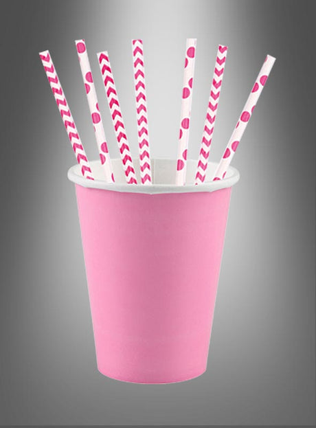 In einem rosa Pappbecher befinden sich sieben Papierstrohhalme in Rosa und Weiß, die jeweils ein einzigartiges Muster wie Streifen, Zickzackmuster und Tupfen vor einem grauen Hintergrund mit Farbverlauf aufweisen. Diese umweltfreundlichen Papierstrohhalme sind die perfekte Wahl für jede Feier.