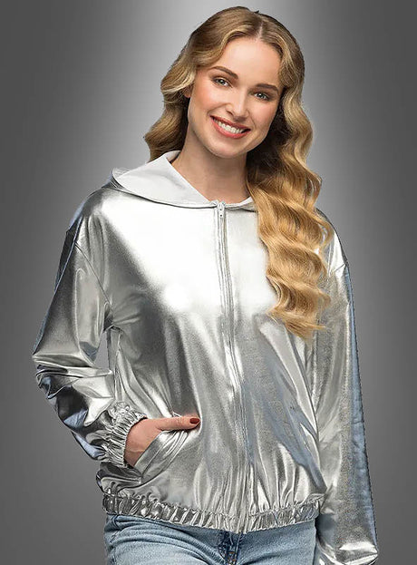 Eine Frau, die den schimmernden silbernen „Disco Blouson Damen“ trägt, steht mit in die Taschen gesteckten Händen vor einem grauen Hintergrund mit Farbverlauf und lächelt in die Kamera – perfekt, um jedem Outfit das klassische Party-Flair der 70er Jahre zu verleihen.