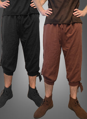Zwei Personen tragen die „Mittelalter Hose Herren“ – kurze Hosen mit Kordelzug in Schwarz und Braun –, die sich perfekt für LARP oder als Teil eines Wikinger-Kostüms eignen. Beide haben die Hände in die Hüften gestemmt und tragen braune Stiefeletten. Die Hosen sind an den Waden zusammengebunden, um einen authentischen mittelalterlichen Look zu erzielen.