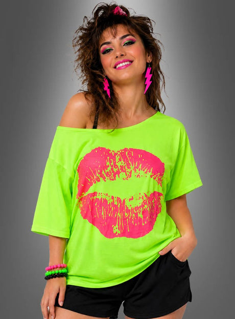 Eine Frau mit toupiertem Haar trägt ein neongrünes 80er-Jahre-Shirt der Marke „Kiss“ mit einem großen rosa Lippen-Motiv, dazu schwarze Shorts, rosa Blitz-Ohrringe und bunte Armbänder; sie steht vor einem schlichten grauen Hintergrund.