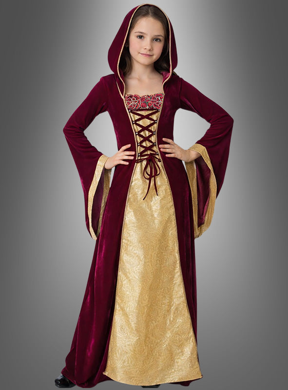 Ein junges Mädchen trägt das Mittelalter-Kleid „Margret“ – ein burgunderrotes Samtkleid im mittelalterlichen Stil mit Schnürung, goldenen Akzenten und einer Kapuze – und steht mit den Händen in die Hüften gestemmt vor einem grauen Hintergrund. Dieses elegante mittelalterliche Kostüm eignet sich perfekt für jeden Anlass.