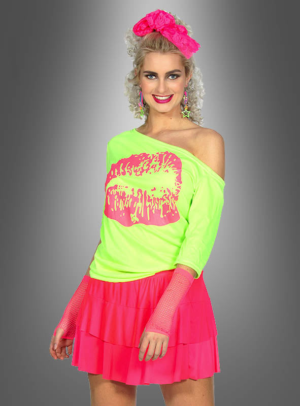 Eine Frau präsentiert das „80er Jahre Shirt Kiss“ – ein übergroßes, neongrünes Top mit freien Schultern und einem auffälligen rosa Lippenprint –, kombiniert mit einem rosa Rock, Netzhandschuhen, auffälligen Ohrringen und einem rosa Stirnband, um vor einem grauen Hintergrund einen Retro-inspirierten Look zu kreieren.