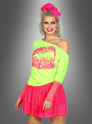 Eine Frau präsentiert das „80er Jahre Shirt Kiss“ – ein übergroßes, neongrünes Top mit freien Schultern und einem auffälligen rosa Lippenprint –, kombiniert mit einem rosa Rock, Netzhandschuhen, auffälligen Ohrringen und einem rosa Stirnband, um vor einem grauen Hintergrund einen Retro-inspirierten Look zu kreieren.