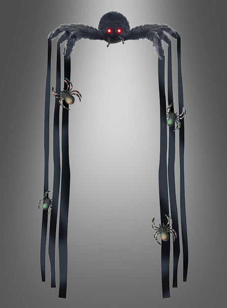 Eine riesige Deko-Spinne (90 cm), mit roten Augen und langen, bandartigen Beinen, verziert mit kleineren Spinnen, hängt vor einem schlichten grauen Hintergrund – perfekt, um Ihrer Halloween-Dekoration einen gruseligen Touch zu verleihen.