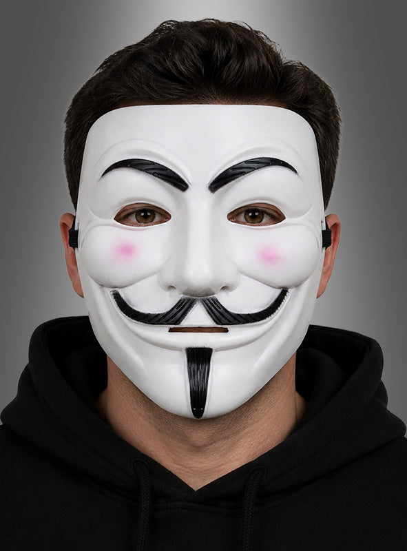 Eine Person, die die „Weiße Maske mit Bart“ trägt – mit schwarzen Details und rosa Wangen im Stil einer Guy-Fawkes-Maske – und einen schwarzen Kapuzenpulli anhat, posiert vor einem grauen Hintergrund mit Farbverlauf.