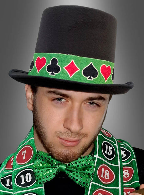 Ein Mann, der einen schwarzen Zylinderhut mit Kartensymbolen, eine grüne Fliege und ein Hutband für Casino-Kostüme trägt und vor einem grauen Hintergrund posiert – als Teil seiner Casino-Kostümaccessoires.