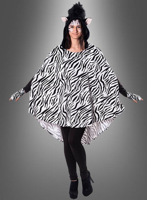 Ein Model trägt den Plüsch-Zebra-Poncho in den Größen XS–XXXL mit auffälligen schwarz-weißen Streifen, dazu einen Kopfschmuck mit Zebra-Ohren, Gesichtsbemalung und schwarze Leggings; es steht mit leicht ausgestreckten Armen vor einem grauen Hintergrund.