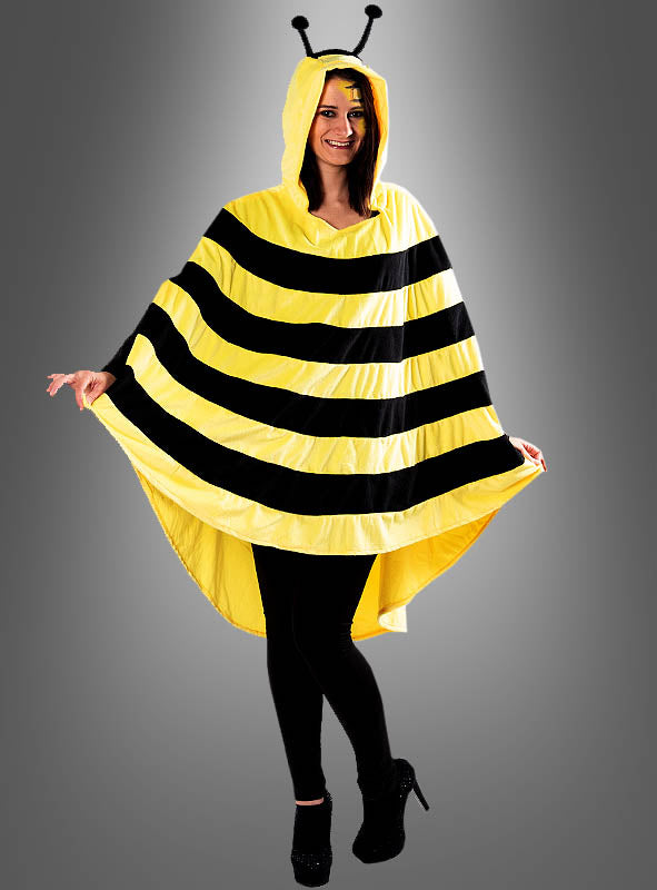 Vor einem grauen Hintergrund steht eine Person, die den „Biene-Poncho aus kuschelweichem Plüsch“ in den Größen S bis XXXL trägt – ein gelb-schwarz gestreiftes Karnevalskostüm mit integrierter Kapuze und Fühlern. Dieser Plüschponcho verleiht jedem Kostüm-Look zum Thema „Biene“ verspielten Charme und kuscheligen Tragekomfort.