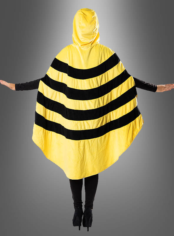 Eine Person steht mit ausgestreckten Armen da und trägt den „Biene Poncho aus kuschelweichem Plüsch S-XXXL“ – einen gelben Plüschumhang mit schwarzen Querstreifen und einer Kapuze, die an eine Hummel erinnert – vor einem grauen Hintergrund mit Farbverlauf, was ihn zur idealen Wahl für ein fröhliches Karnevalskostüm macht.