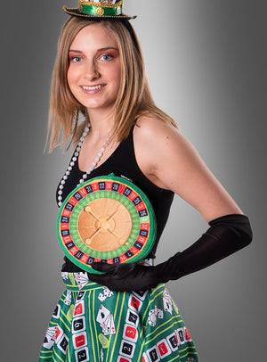 Vor einem grauen Hintergrund steht eine Frau in einem farbenfrohen Casino-Kostüm mit einem Roulette-Rad-Motiv auf der Brust, einem Rock mit Spielkartenmustern, schwarzen Handschuhen, einer Perlenkette und einem kleinen grünen Hut. Abgerundet wird ihr Look durch die stilvolle „Roulette-Handtasche zum Kostüm“ – das perfekte Accessoire für jede Las-Vegas-Party.