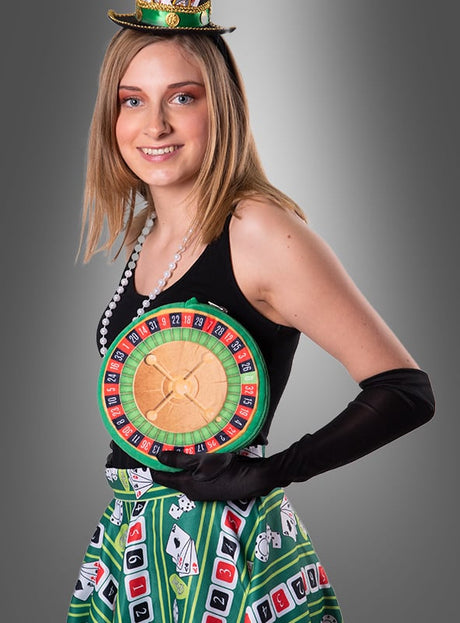 Vor einem grauen Hintergrund steht eine Frau in einem farbenfrohen Casino-Kostüm mit einem Roulette-Rad-Motiv auf der Brust, einem Rock mit Spielkartenmustern, schwarzen Handschuhen, einer Perlenkette und einem kleinen grünen Hut. Abgerundet wird ihr Look durch die stilvolle „Roulette-Handtasche zum Kostüm“ – das perfekte Accessoire für jede Las-Vegas-Party.