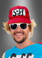 Eine Person lächelt vor einem grauen Hintergrund mit Farbverlauf und trägt eine rote „Mütze Suffman Bier Mann Festival“-Kappe mit der Aufschrift „Suff“, eine weiße Sonnenbrille, eine blonde Perücke und ein blaues Hemd.