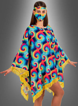 Eine Frau trägt den „Hippie-Poncho für Damen mit Batik-Muster“, der sich durch ein farbenfrohes Batik-Design mit gelben Fransen auszeichnet, sowie eine dazu passende Gesichtsmaske und ein Stirnband, während sie vor einem grauen Hintergrund mit Farbverlauf steht.