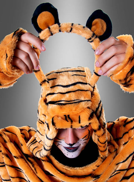Eine Person, die den „Tiger-Poncho aus hochwertigem Plüsch S-XXXL“ trägt, hält ein passendes Stirnband mit Tigerohren über den Kopf, während sie vor einem grauen Farbverlaufshintergrund nach unten blickt – die perfekte Inspiration für Ihr nächstes Karnevals-Gruppenkostüm oder einen auffälligen Tiger-Poncho-Look.