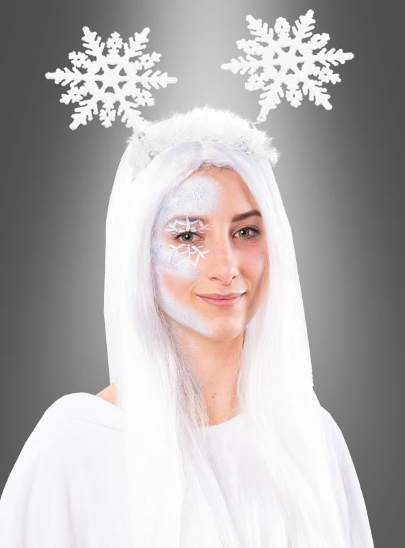 Eine Person mit langen weißen Haaren, in weiße Kleidung gekleidet, mit Schneeflocken-Gesichtsbemalung und einem Stirnband mit zwei großen Schneeflocken an Federn, trägt als Teil ihres Karnevalskostüms einen wandelbaren weißen Poncho aus Plüsch in den Größen S bis XXXL vor einem grauen Hintergrund.