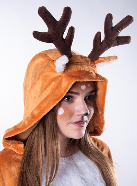 Vor einem einfarbigen Hintergrund ist eine Person zu sehen, die den „Kuschelweichen Reh-Poncho“ (S–XXXL) trägt, der eine braune Kapuze mit Geweih und weiße Punkte im Gesicht aufweist, um einem Rentier zu ähneln.