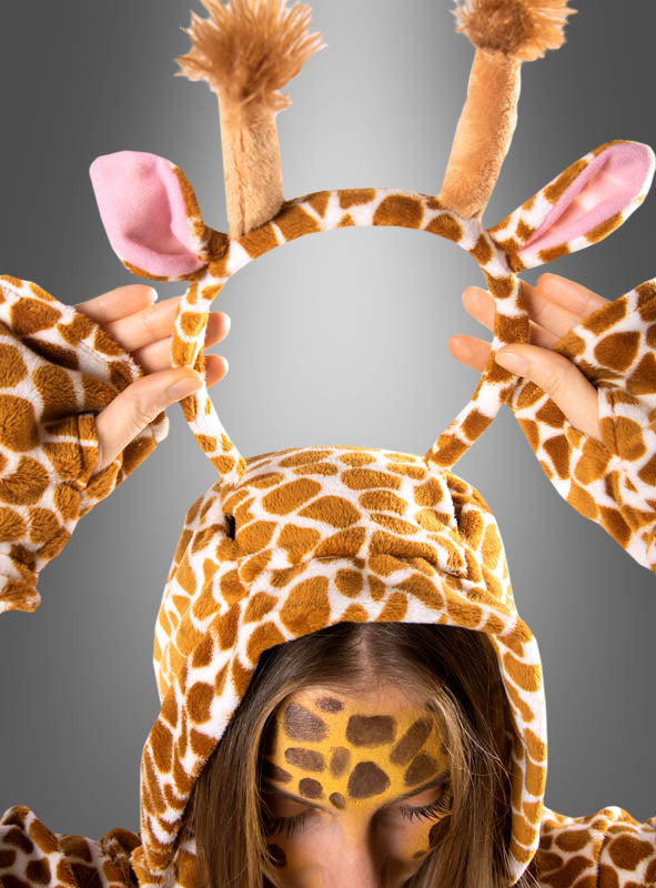 Eine Person, die den „Plüsch-Giraffen-Poncho mit Haarreif S–XXXL“ trägt und sich das Gesicht bemalt hat, hält das mitgelieferte Stirnband mit Giraffenohren und -hörnern vor einem grauen Hintergrund hoch – ideal für Ihre nächste Safari-Mottoparty oder als verspieltes Tierponcho-Kostüm.