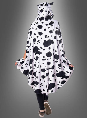 Eine Person steht mit dem Rücken zur Kamera vor einem grauen Hintergrund und trägt den „Kuh-Poncho aus Plüsch mit Eutertasche“ (Größen S–XXXL), ein kuscheliges Cape mit Kapuze im schwarz-weißen Kuhmuster.
