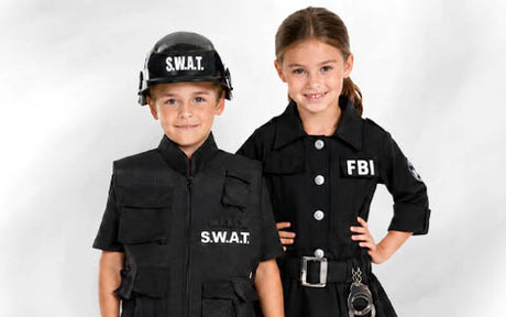 Zwei Kinder in schwarzen Polizeikostümen stehen nebeneinander; das eine trägt eine SWAT-Weste und einen Helm, das andere ein FBI-Kleid mit Dienstmarke und Spielzeug-Handschellen.