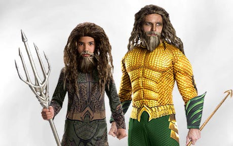 Zwei Personen in Aquaman-Kostümen stehen nebeneinander; die eine hält einen Dreizack, die andere einen goldenen Haken, beide tragen lange Perücken und Bärte.