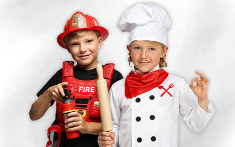 Zwei Kinder in Kostümen: eines als Feuerwehrmann mit einem Feuerlöscher, das andere als Koch mit einem Nudelholz, einer Kochmütze und einem roten Halstuch.