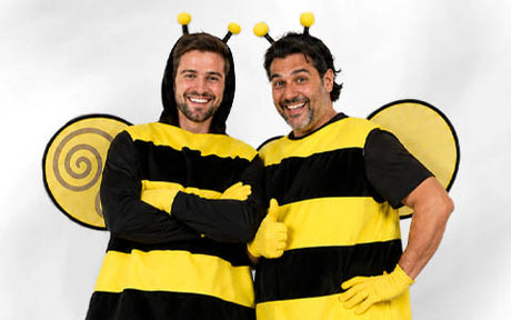 Zwei Erwachsene in schwarz-gelben Bienenkostümen mit Fühlern und Flügeln posieren lächelnd vor einem schlichten weißen Hintergrund.