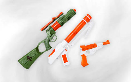 Drei Spielzeugpistolen aus Kunststoff – eine grüne mit Zielfernrohr, eine orange-weiße mit Pumpmechanismus und eine kleine orange-weiße Pistole – sind vor einem weißen Hintergrund ausgestellt.
