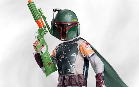Eine Person in einem Boba-Fett-Kostüm und -Helm, die einen großen grün-orangefarbenen Spielzeugblaster in der Hand hält und einen grauen Umhang trägt, vor einem schlichten Hintergrund.