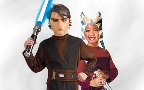 Zwei Kinder tragen „Star Wars“-Kostüme: Das eine ist als Anakin Skywalker verkleidet und hält ein blaues Lichtschwert in der Hand, das andere als Ahsoka Tano, lächelt und hält ein kleines Lichtschwert in der Hand.