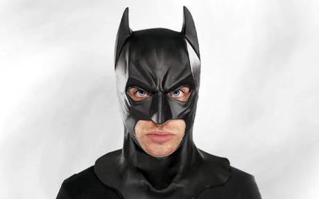 Eine Person in einem schwarzen Batman-Kostüm und mit einer Maske, die vor einem schlichten weißen Hintergrund direkt in die Kamera blickt.