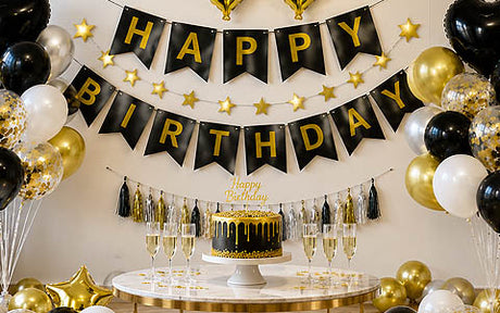 Schwarz-goldene „Happy Birthday“-Dekoration mit Luftballons, einer Torte und Champagnergläsern, die auf einem runden Tisch angeordnet sind.