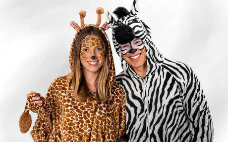 Zwei Personen in Tierkostümen – eine als Giraffe und eine als Zebra – stehen lächelnd nebeneinander vor einem schlichten weißen Hintergrund.