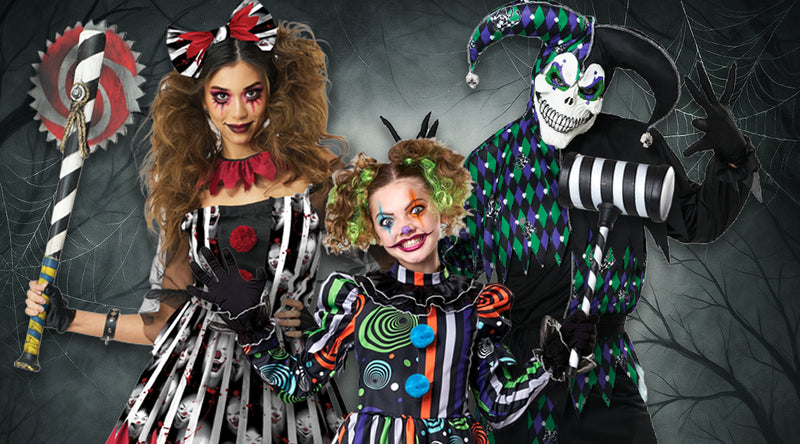 Drei Personen in gruseligen Clownskostümen mit buntem Make-up posieren vor einem Hintergrund mit Spinnweben. Eine hält eine Axt in der Hand, eine andere einen Hammer, und alle tragen gemusterte und gestreifte Outfits.