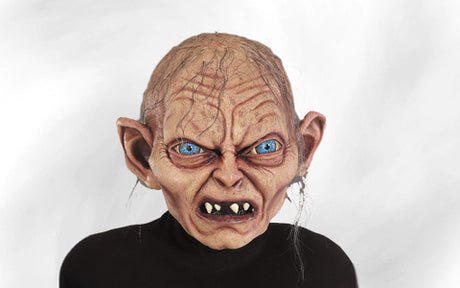 Eine Person, die eine Maske mit übertriebenen Gesichtszügen trägt, mit blauen Augen, spitzen Ohren, einer Glatze und ungleichmäßigen Zähnen, vor einem schlichten weißen Hintergrund.