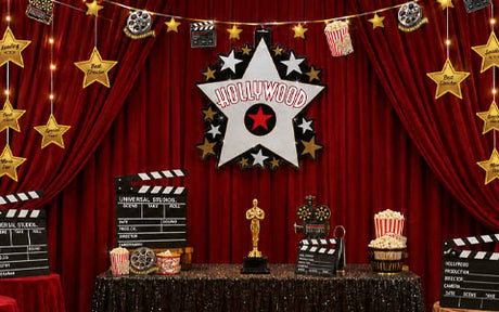 Partydekoration im Hollywood-Stil mit einem großen weißen Sternschild, roten Vorhängen, goldenen Stern-Dekorationen, Filmrollen, Popcorn, Filmklappen und einer goldenen Oscar-Statue auf einem glitzernden schwarzen Tisch.
