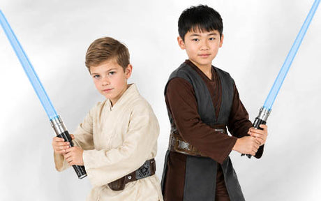 Zwei Kinder, die als Jedi aus „Star Wars“ verkleidet sind, stehen nebeneinander und halten jeweils ein blaues Lichtschwert vor einem schlichten weißen Hintergrund.